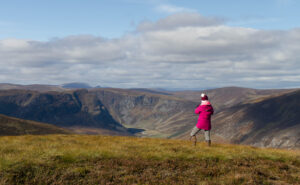 Photo of a female figure stood on top of a hill looking out at the view