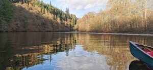 Photo of the river Garry in Scotland. The trees have no leaves on as it's winter. To the right of the image is the front of a canoe